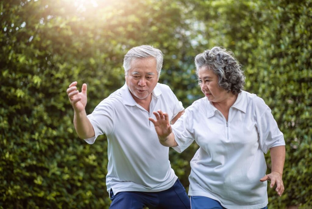 Senior man showing senior woman how to do tai chi outside.