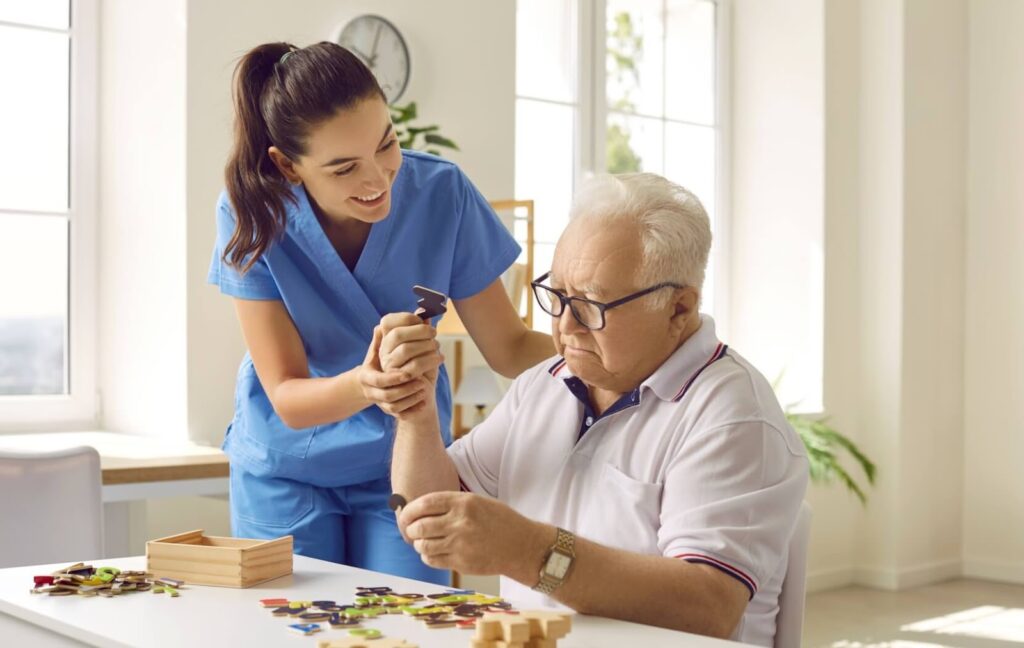 A memory care staff member helps their patient complete a puzzle in a shared activity room to help maintain cognitive function.