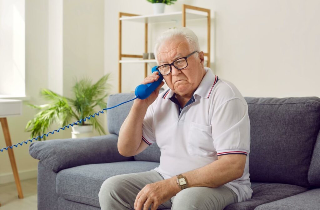 A senior holds a landline phone backward up to their ear, demonstrating early signs of dementia
