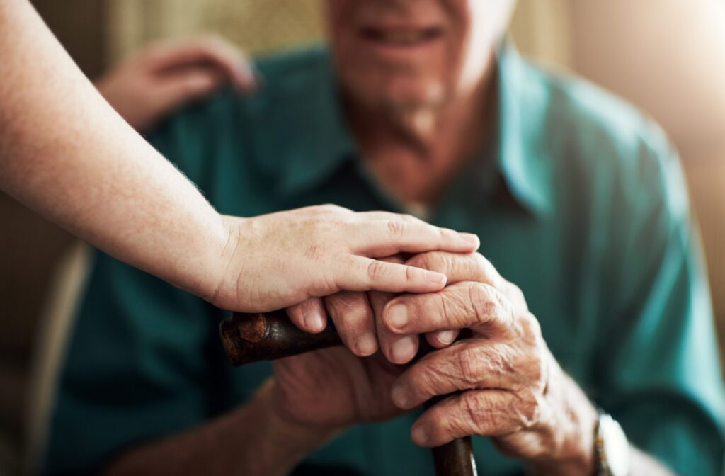 A close-up of the hands of an older adult holding a wooden cane and a caregiver giving them support in a personal care community in Kentucky.