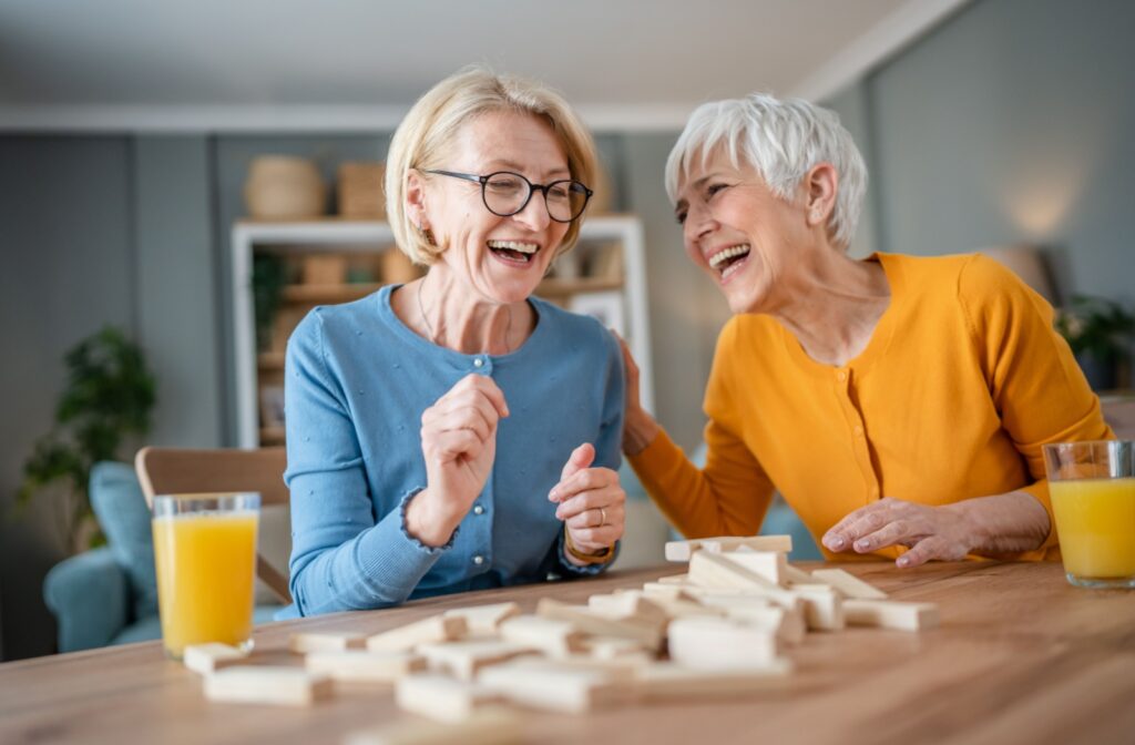 Two seniors laugh and play a board game in senior living.
